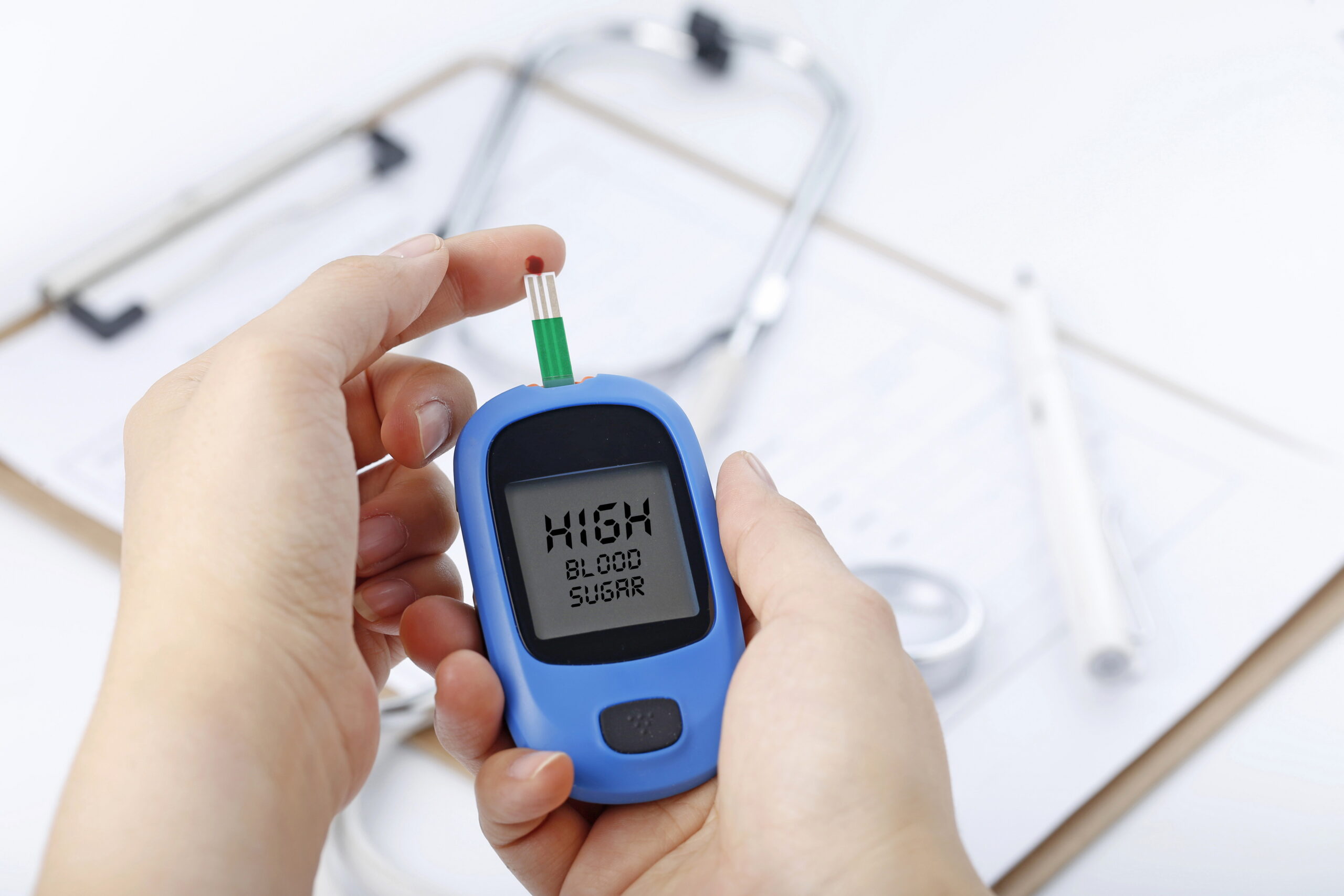 Hand holding a blood glucose meter measuring blood sugar, the background is a stethoscope and chart file Hand holding a blood glucose meter measuring blood sugar, the background is a stethoscope and chart file