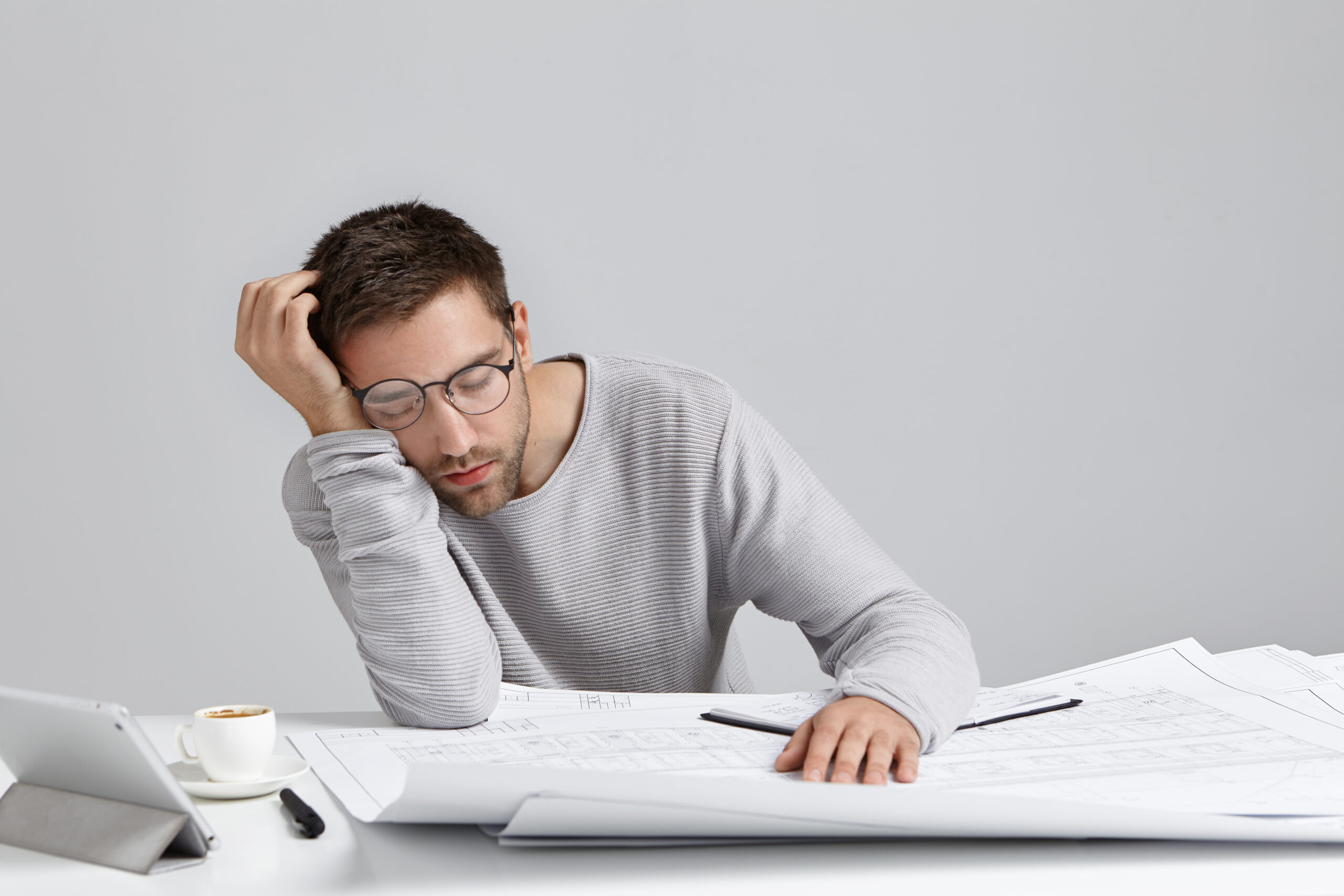 Tired young attractive man sleeps at work place, has much work, being fatigue and exhausted, isolated over white studio background. Sleepy male engineer has deadline, busy all day, has sleppless night Tired young attractive man sleeps at work place, has much work, being fatigue and exhausted, isolated over white studio background. Sleepy male engineer has deadline, busy all day, has sleppless night