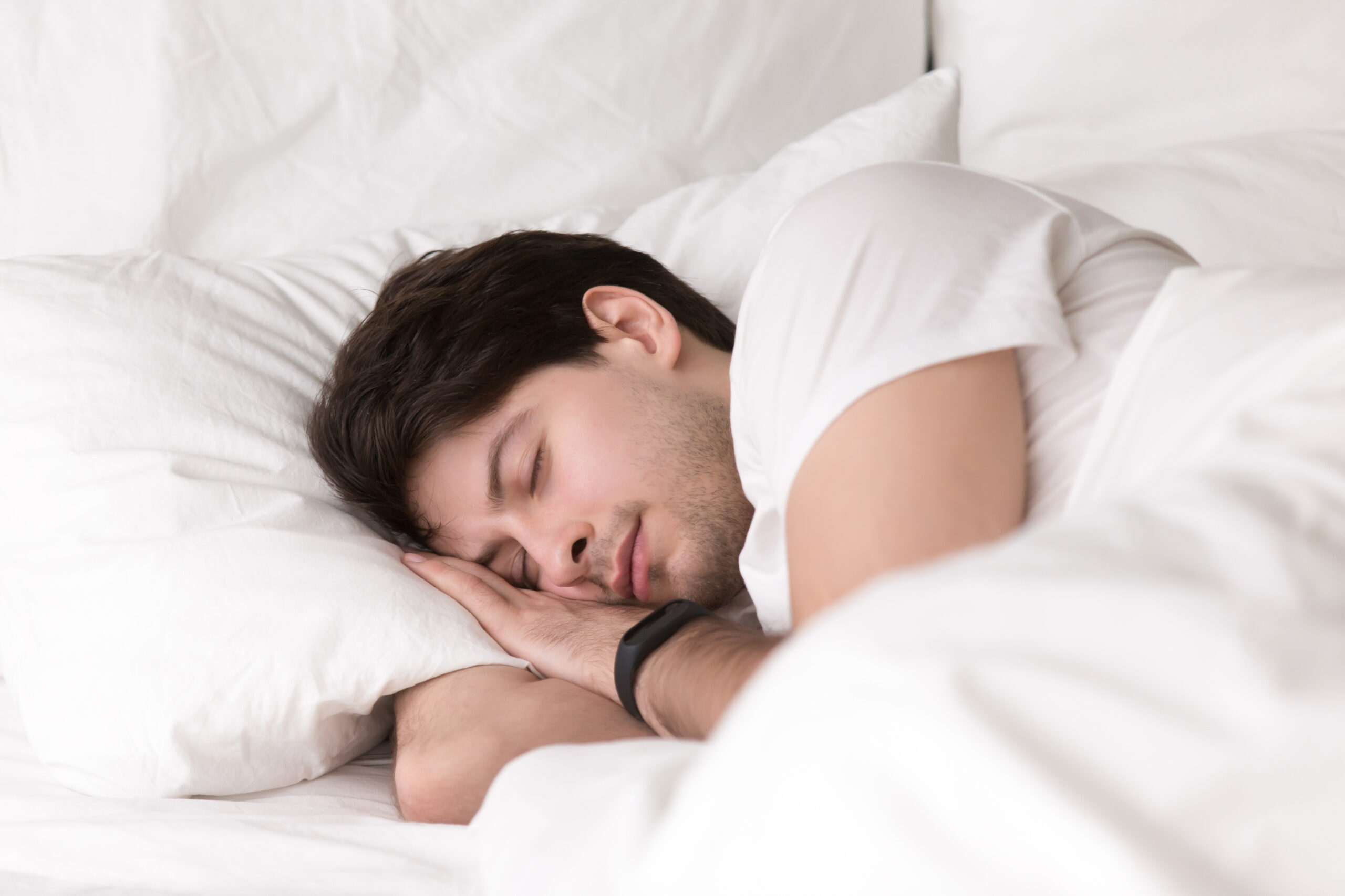 Young guy sleeping in bed wearing smartwatch or sleep tracker Young guy sleeping in bed wearing smartwatch or sleep tracker