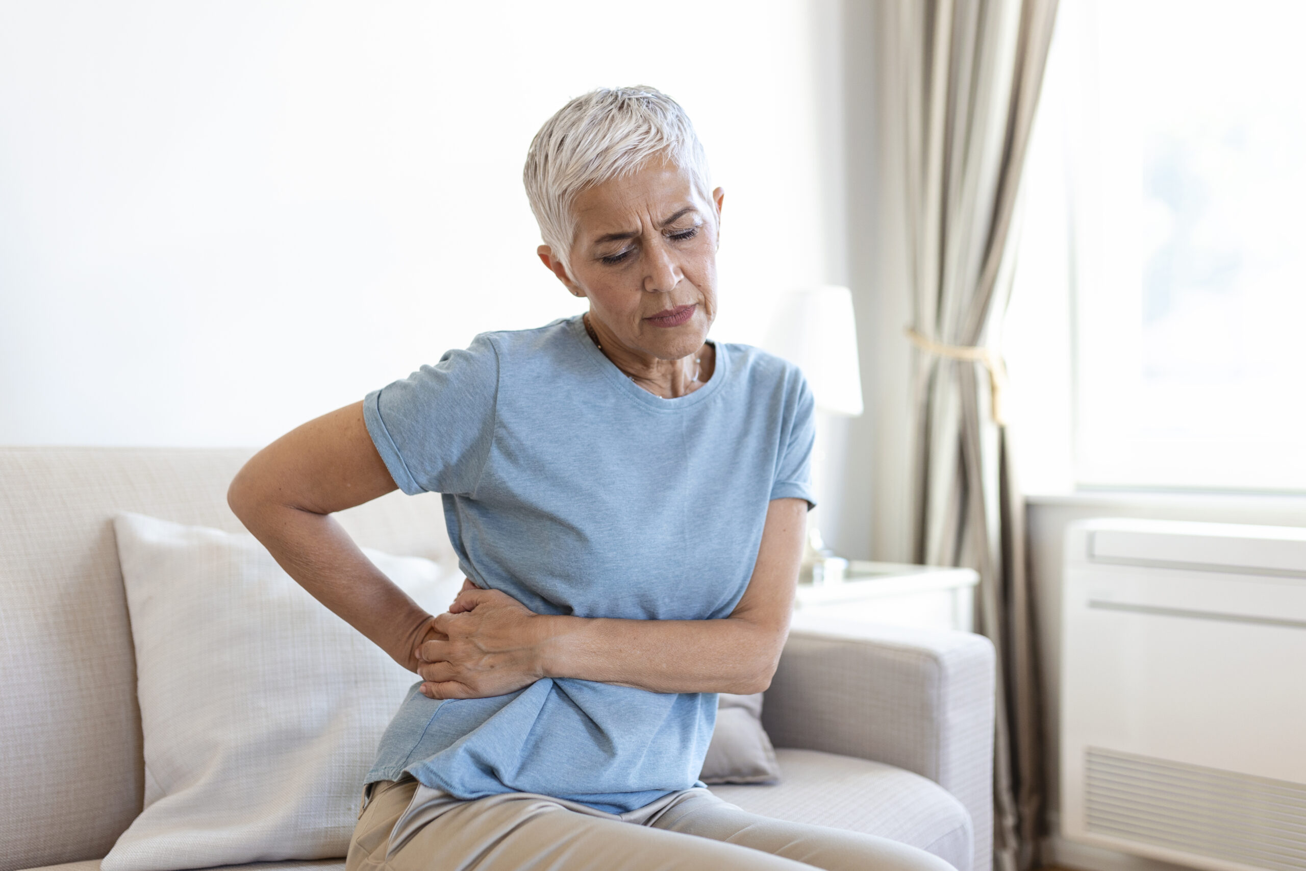 Unhealthy mature woman holding belly, feeling discomfort, health problem concept, unhappy older female sitting on bed, suffering from stomachache, food poisoning, gastritis, abdominal pain, climax Unhealthy mature woman holding belly, feeling discomfort, health problem concept, unhappy older female sitting on bed, suffering from stomachache, food poisoning, gastritis, abdominal pain, climax