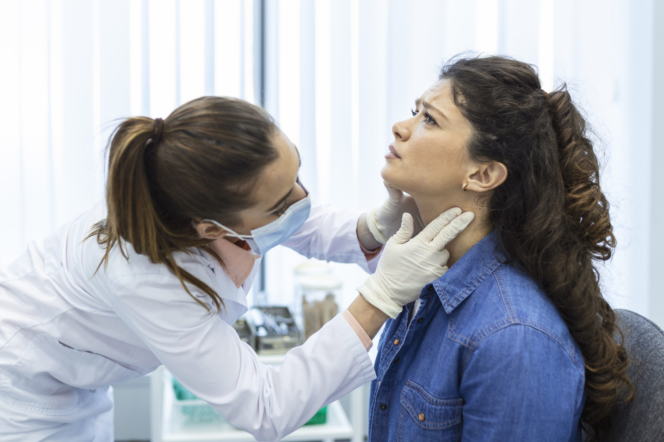 Endocrinologist examining throat of young woman in clinic. Women with thyroid gland test . Endocrinology, hormones and treatment. Inflammation of the sore throat Endocrinologist examining throat of young woman in clinic. Women with thyroid gland test . Endocrinology, hormones and treatment. Inflammation of the sore throat
