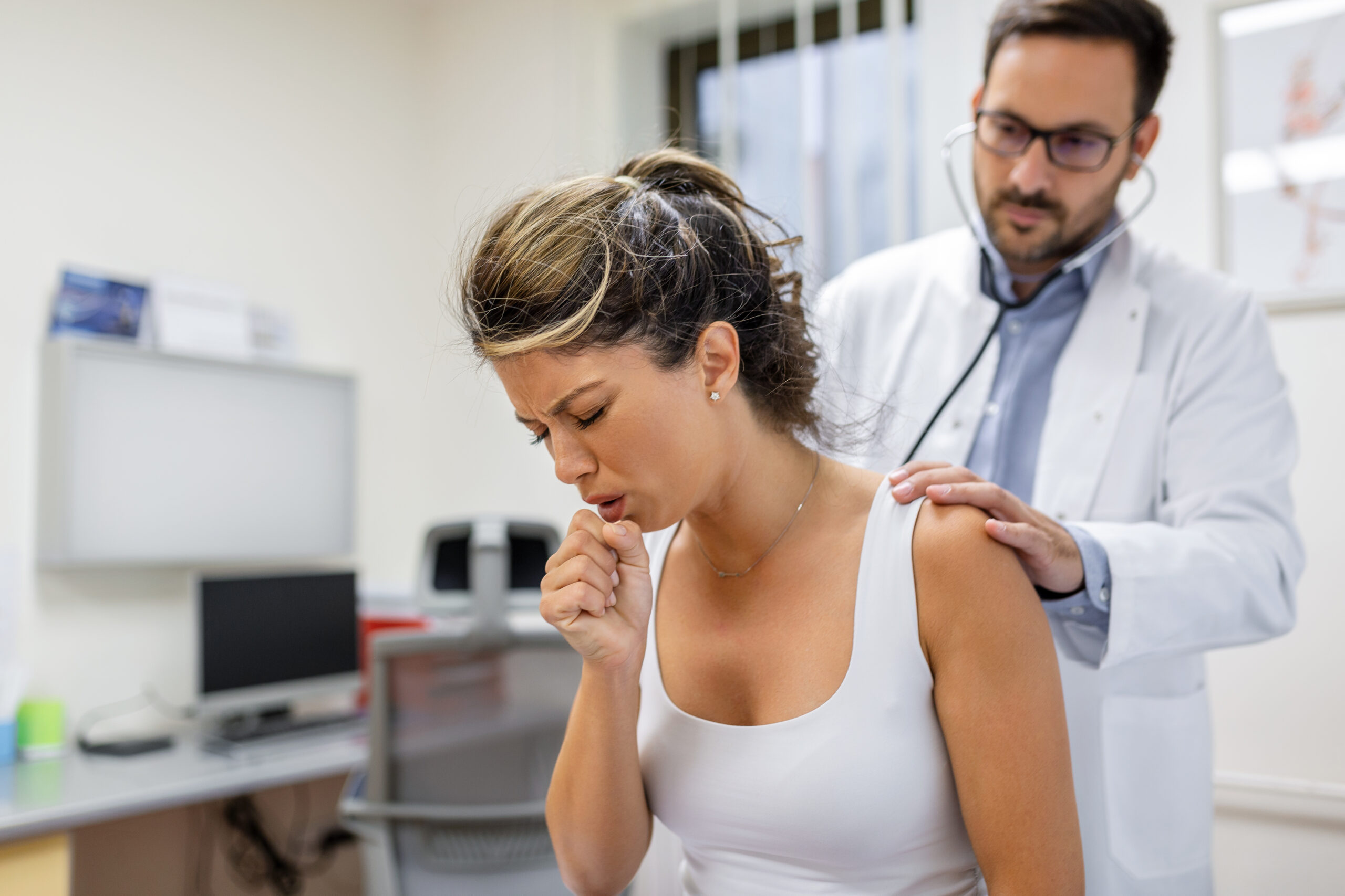 Young female patient in the clinic suffered from pneumonia, she is coughing the doctor listens to the wheezing in the lungs with a stethoscope. Young female patient in the clinic suffered from pneumonia, she is coughing the doctor listens to the wheezing in the lungs with a stethoscope.