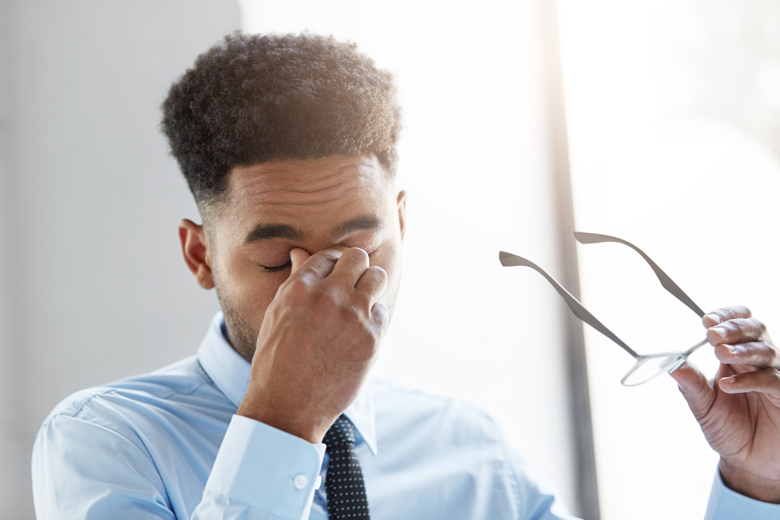 Frustrated young Afro American businessman feeling stressed after hard work, having tired expression, keeping his hand on eyes, resting for minute. Overworked mixed race male feeling stressed Frustrated young Afro American businessman feeling stressed after hard work, having tired expression, keeping his hand on eyes, resting for minute. Overworked mixed race male feeling stressed