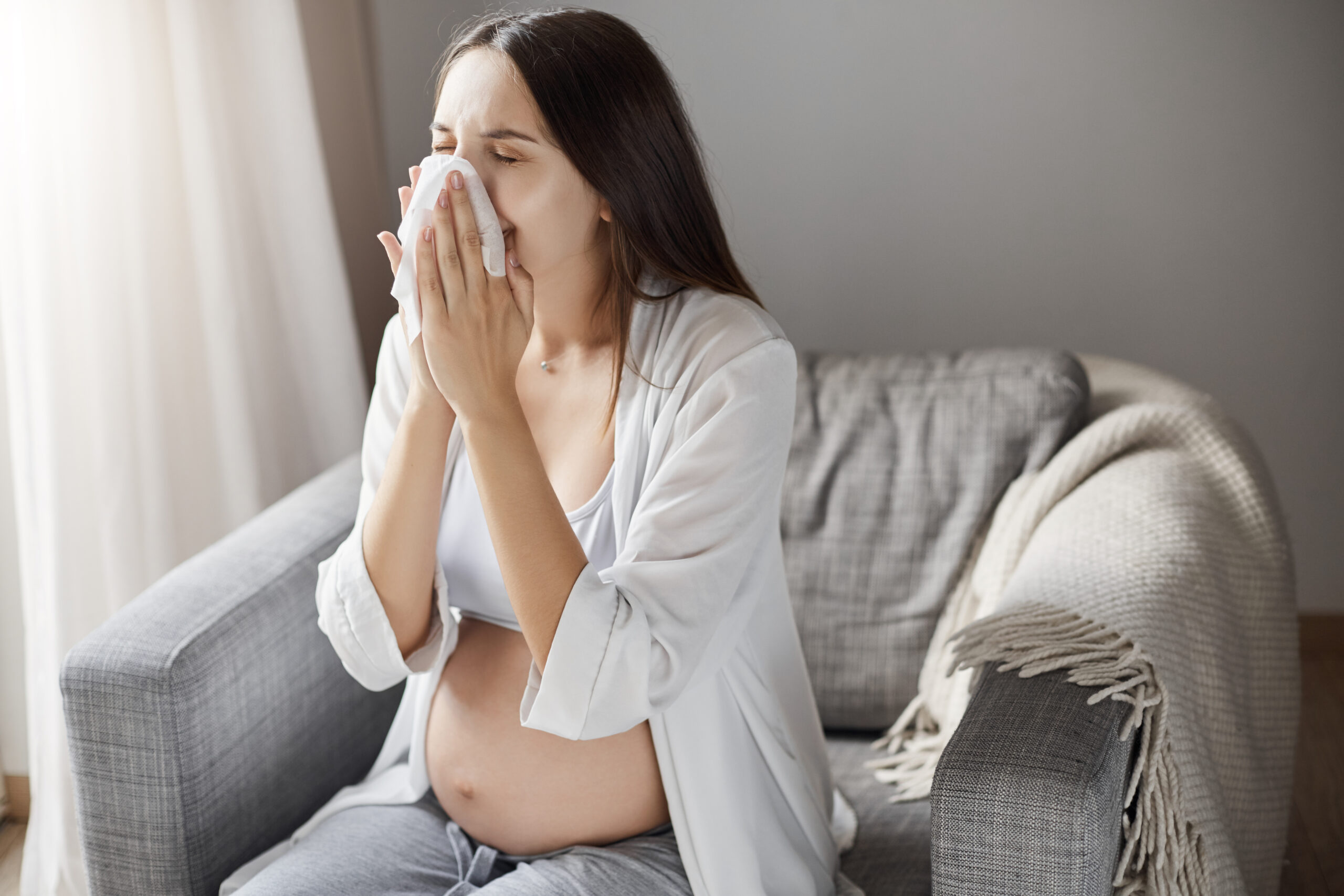 Young pregnant woman suffering from flu. Coughing and using a tissue. Keeping healthy pregnancy is hard. Young pregnant woman suffering from flu. Coughing and using a tissue. Keeping healthy pregnancy is hard.