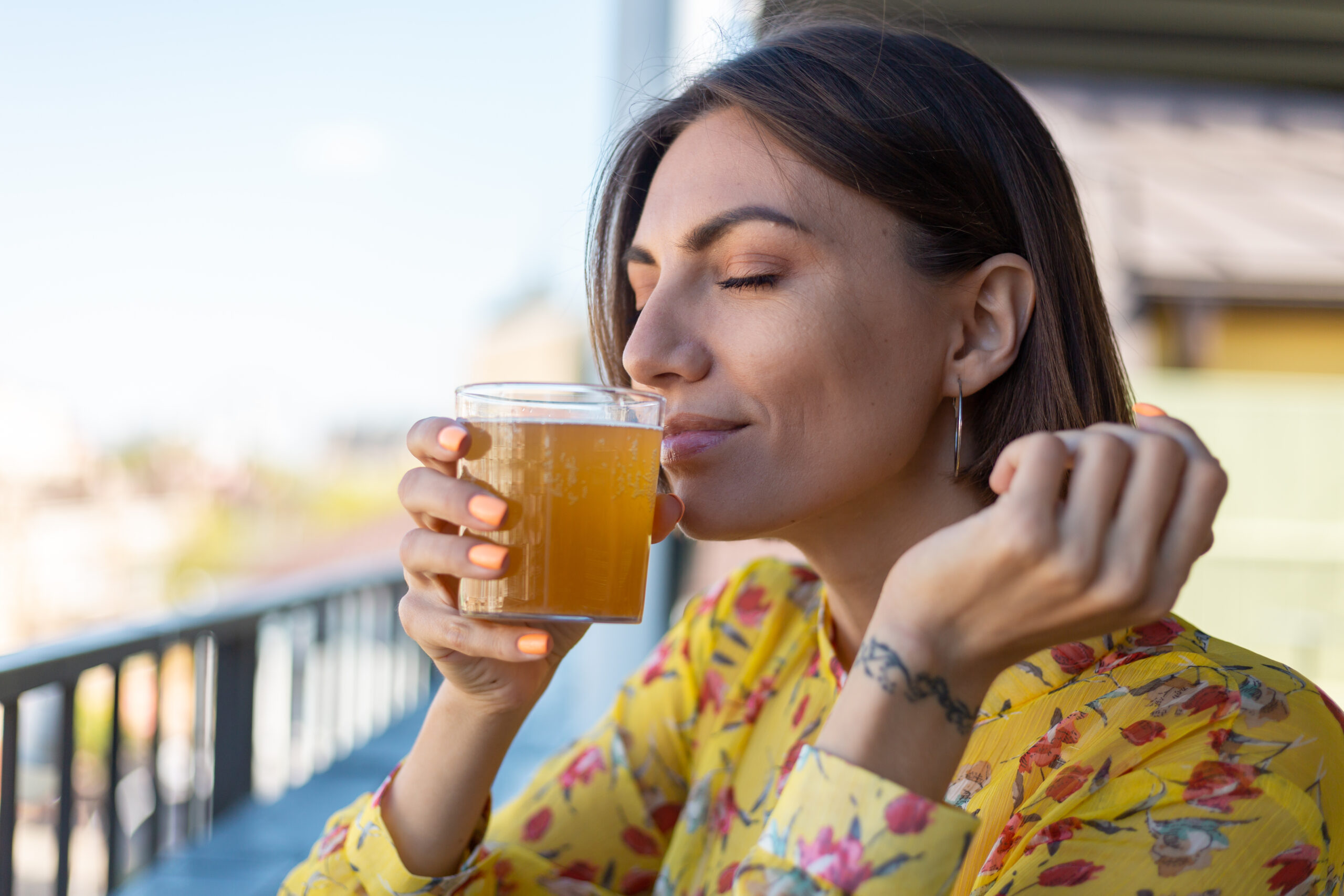Woman in dress in summer cafe enjoying cool kombucha glass of beer sniffing smell with eyes closed Woman in dress in summer cafe enjoying cool kombucha glass of beer sniffing smell with eyes closed