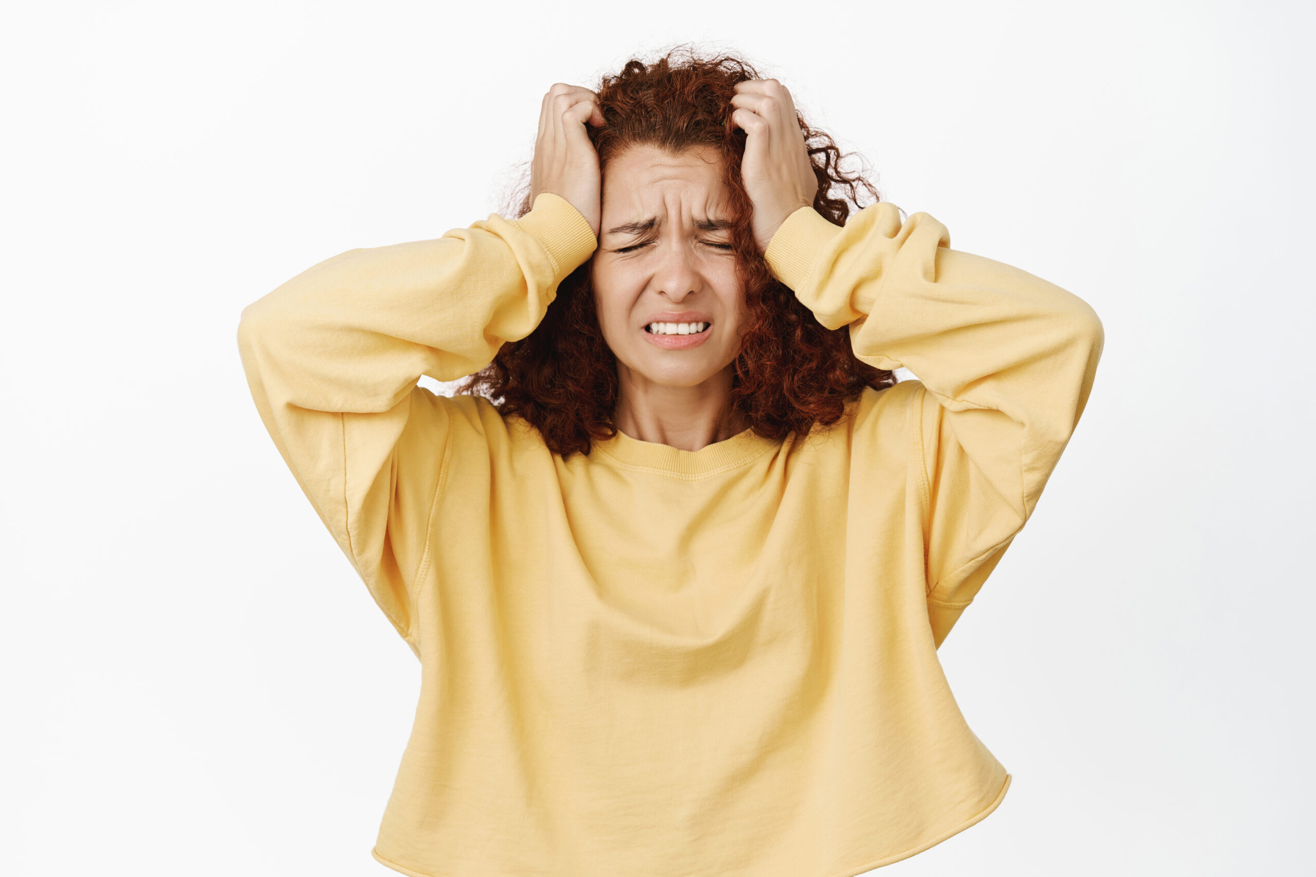 Image of troubled, frustrated redhead woman hold hands on head and grimacing in despair, distressed, bad concerning news, standing anxious over white background