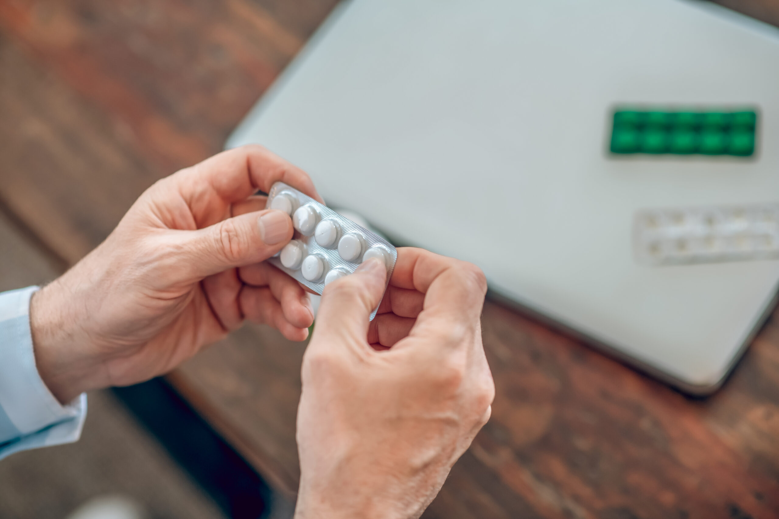 Man seated at a wooden table taking a prescription drug Man seated at a wooden table taking a prescription drug