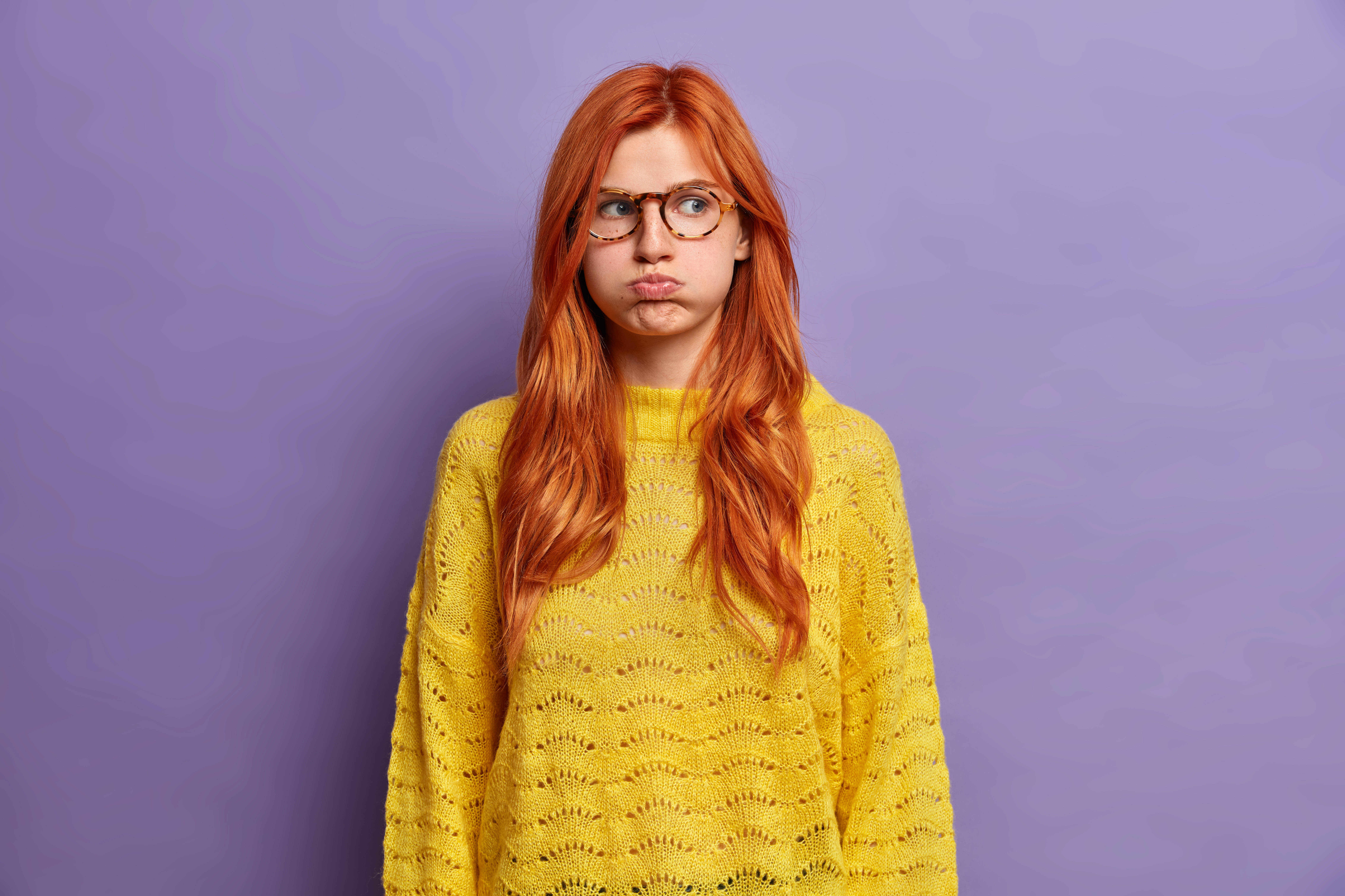 Indoor shot of ginger offended young woman blows cheeks and makes unhappy grimace holds air has moody expression wears yellow sweater displeased with awful situation happened shows bad character Indoor shot of ginger offended young woman blows cheeks and makes unhappy grimace holds air has moody expression wears yellow sweater displeased with awful situation happened shows bad character