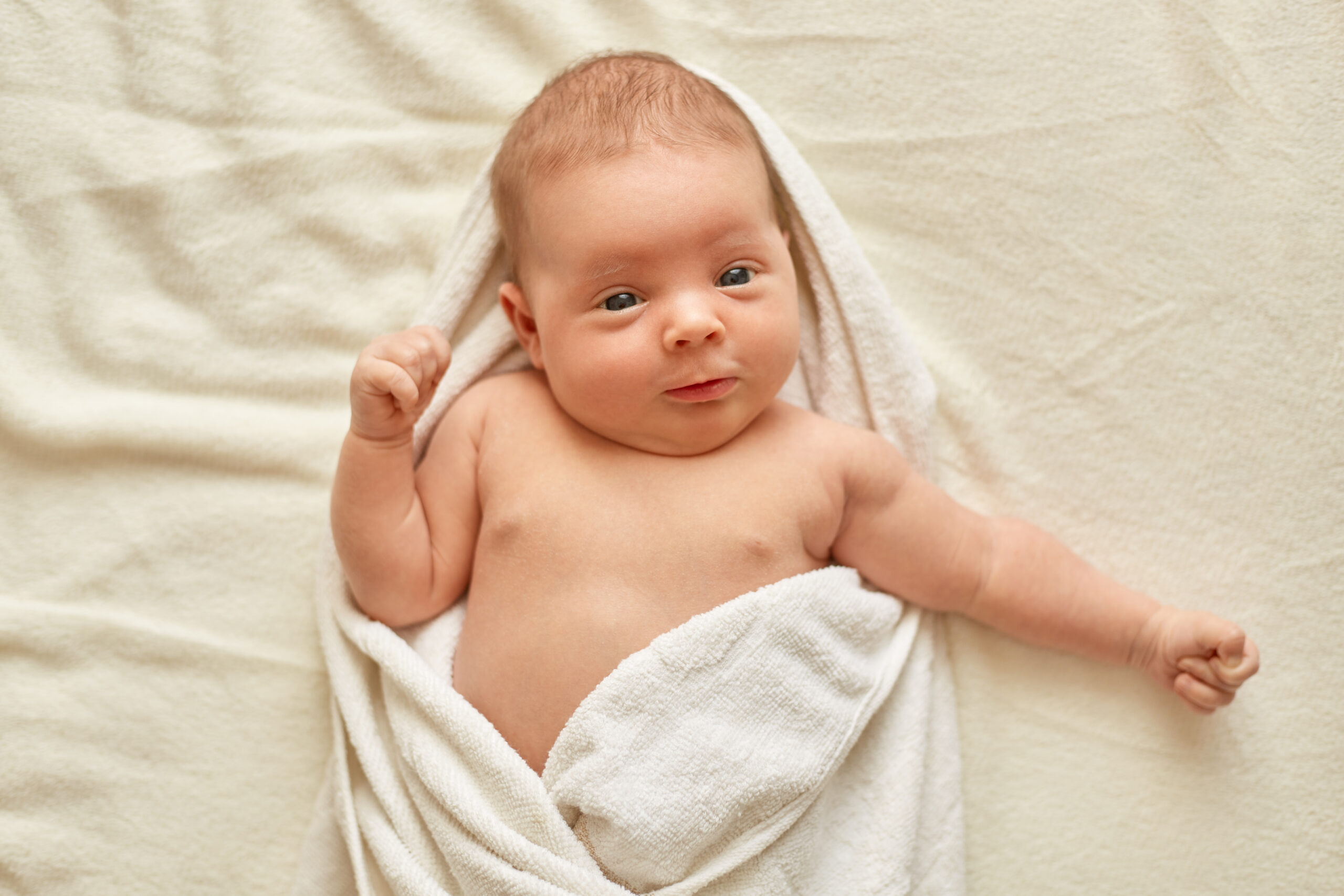 Baby child after bath lying on bed on white blanket, looking at camera, being wrapped in towel, infant after shower, charming newborn kid. Baby child after bath lying on bed on white blanket, looking at camera, being wrapped in towel, infant after shower, charming newborn kid.