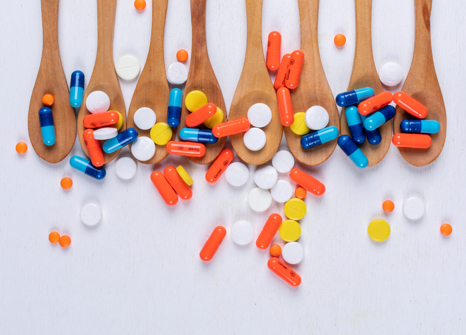 Colorful pills in wooden spoons top view on a white background Colorful pills in wooden spoons top view on a white background