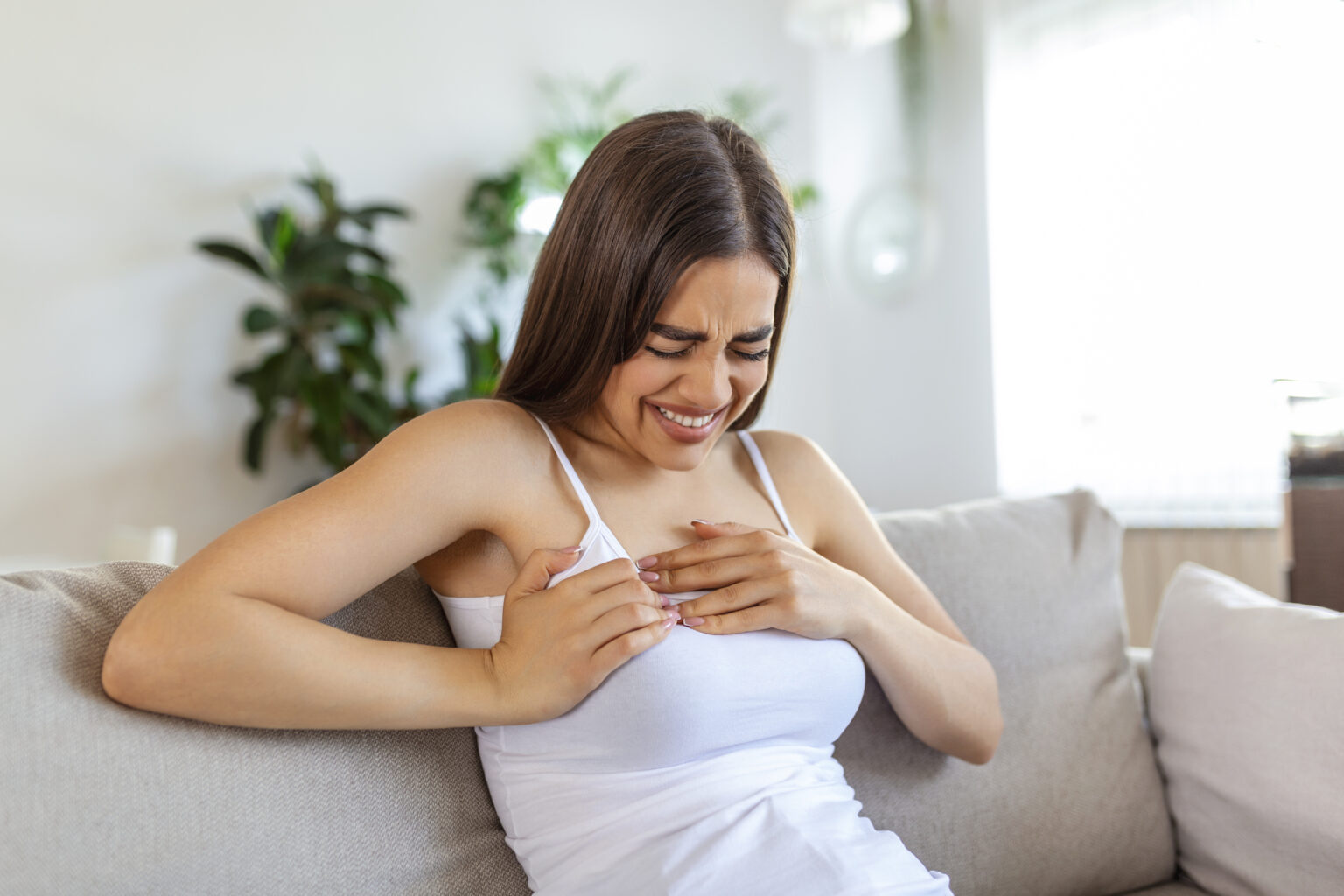 Woman sitting with strong chest pain and hands touching her chest while having trouble at home, Heart attack or heart failure symptom Woman sitting with strong chest pain and hands touching her chest while having trouble at home, Heart attack or heart failure symptom