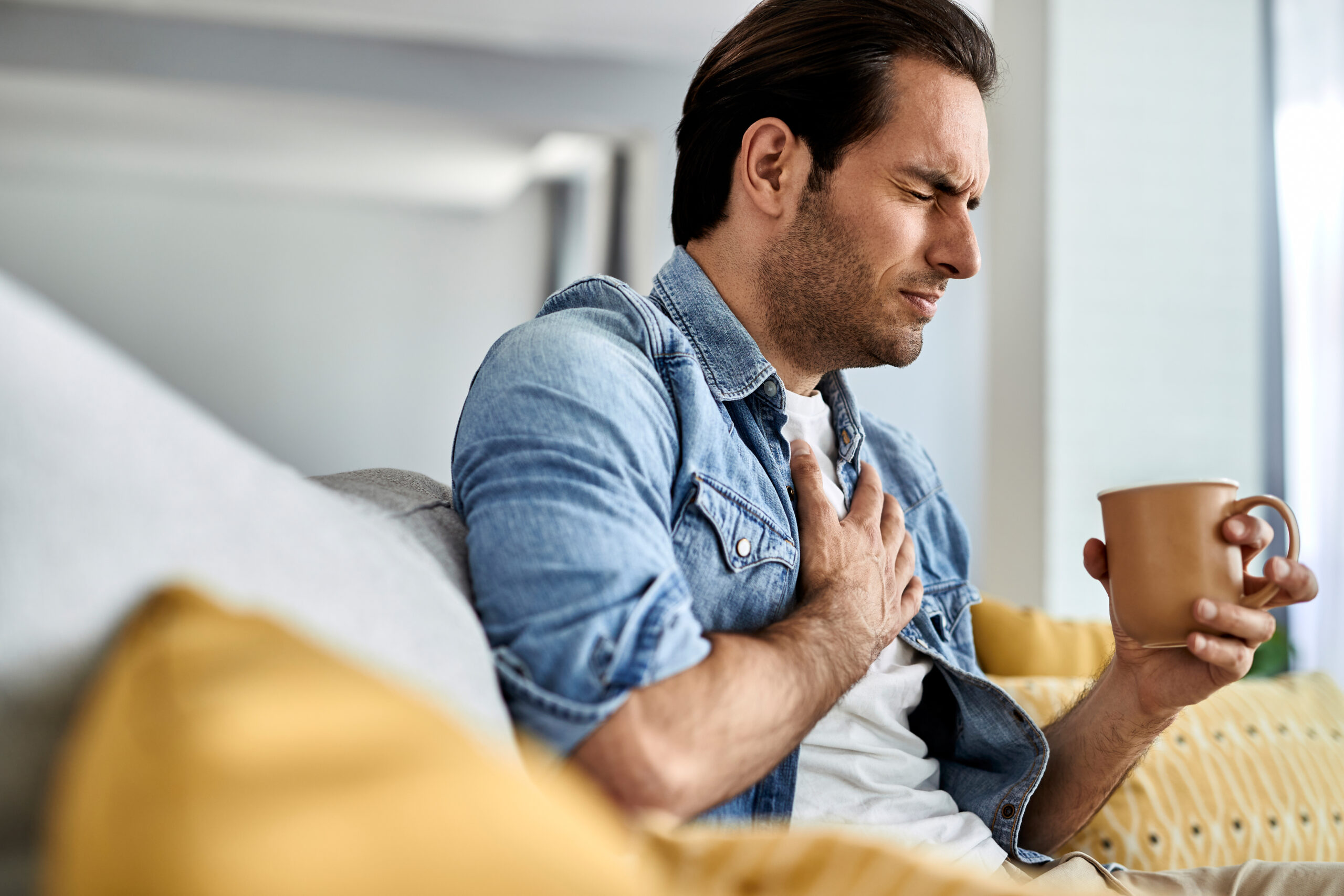 Young man having a chest pain while drinking tea at home. Young man having a chest pain while drinking tea at home.