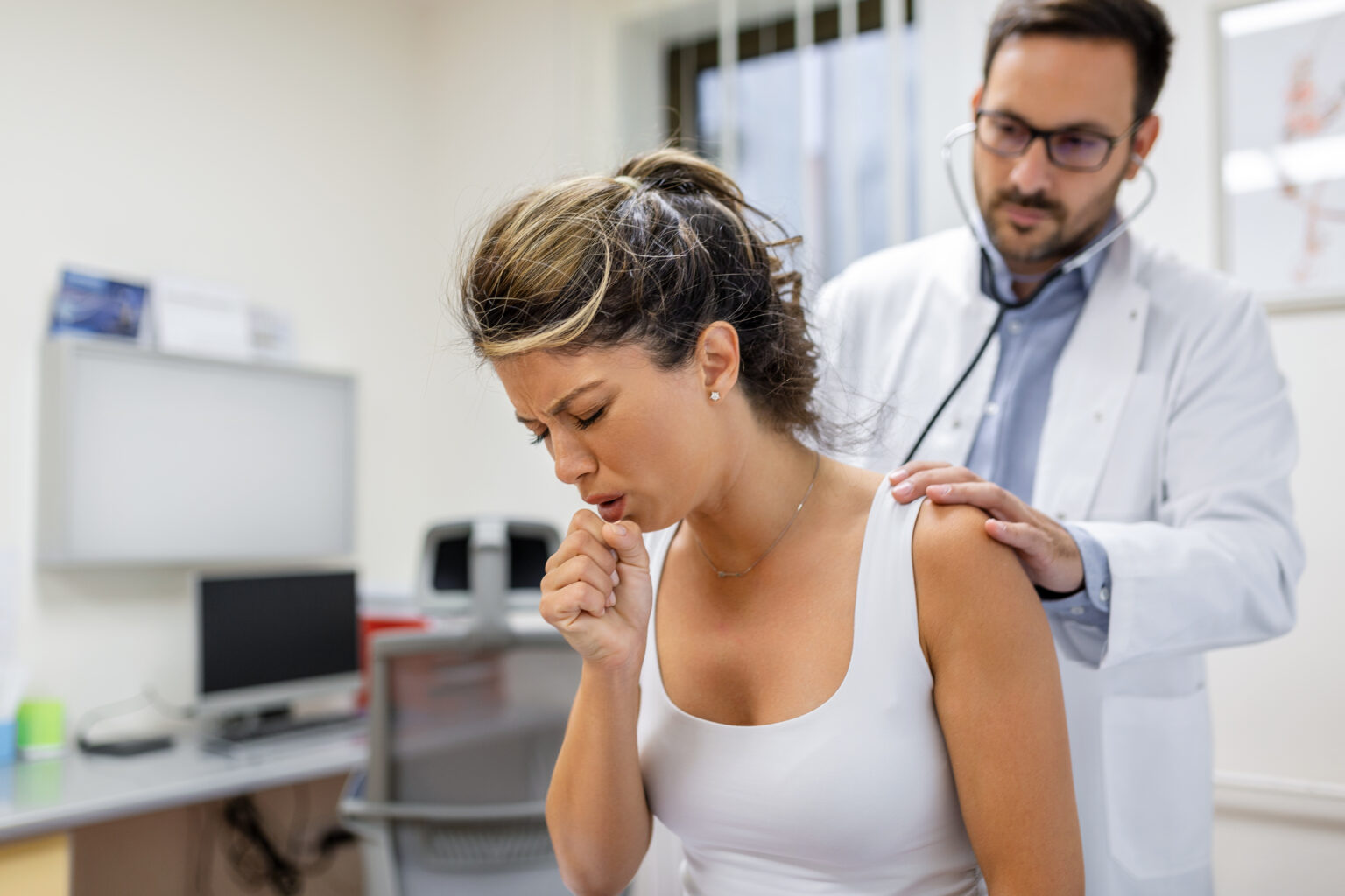 Young female patient in the clinic suffered from pneumonia, she is coughing the doctor listens to the wheezing in the lungs with a stethoscope. Young female patient in the clinic suffered from pneumonia, she is coughing the doctor listens to the wheezing in the lungs with a stethoscope.
