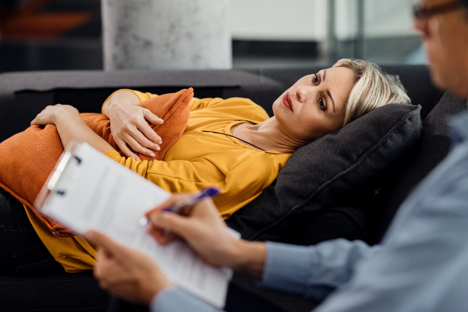 Thoughtful woman lying down on psychiatrist’s couch during an ap Thoughtful woman lying down on psychiatrist’s couch during an ap