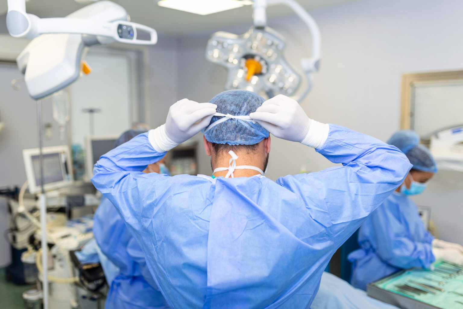 Rear view of male surgeon wearing surgical mask in operation theater at hospital Rear view of male surgeon wearing surgical mask in operation theater at hospital