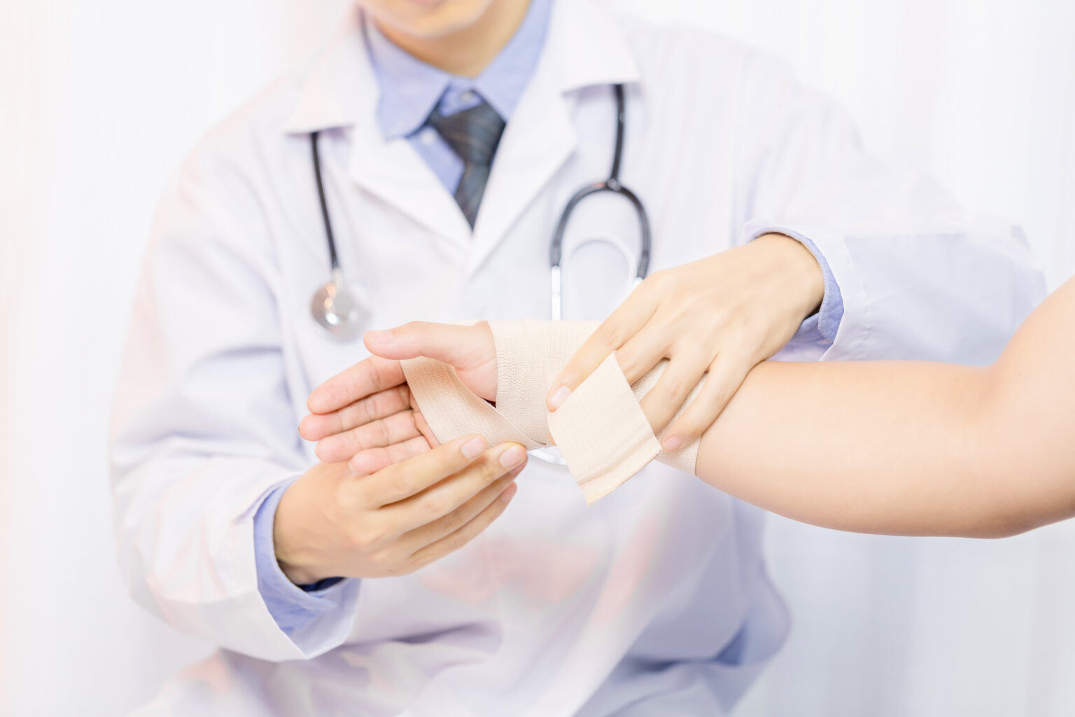 Male doctor putting gauze on young man’s hand in clinic, closeup Male doctor putting gauze on young man’s hand in clinic, closeup