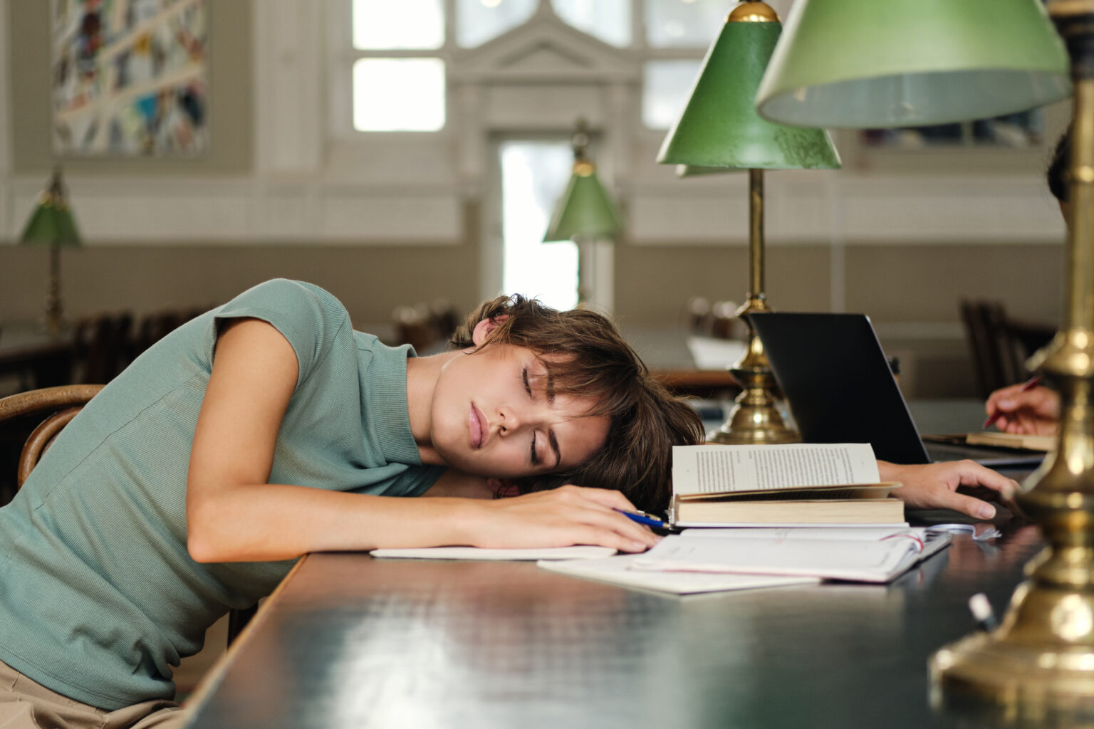 Young tired female student sleeping on desk with books around du Young tired female student sleeping on desk with books around du