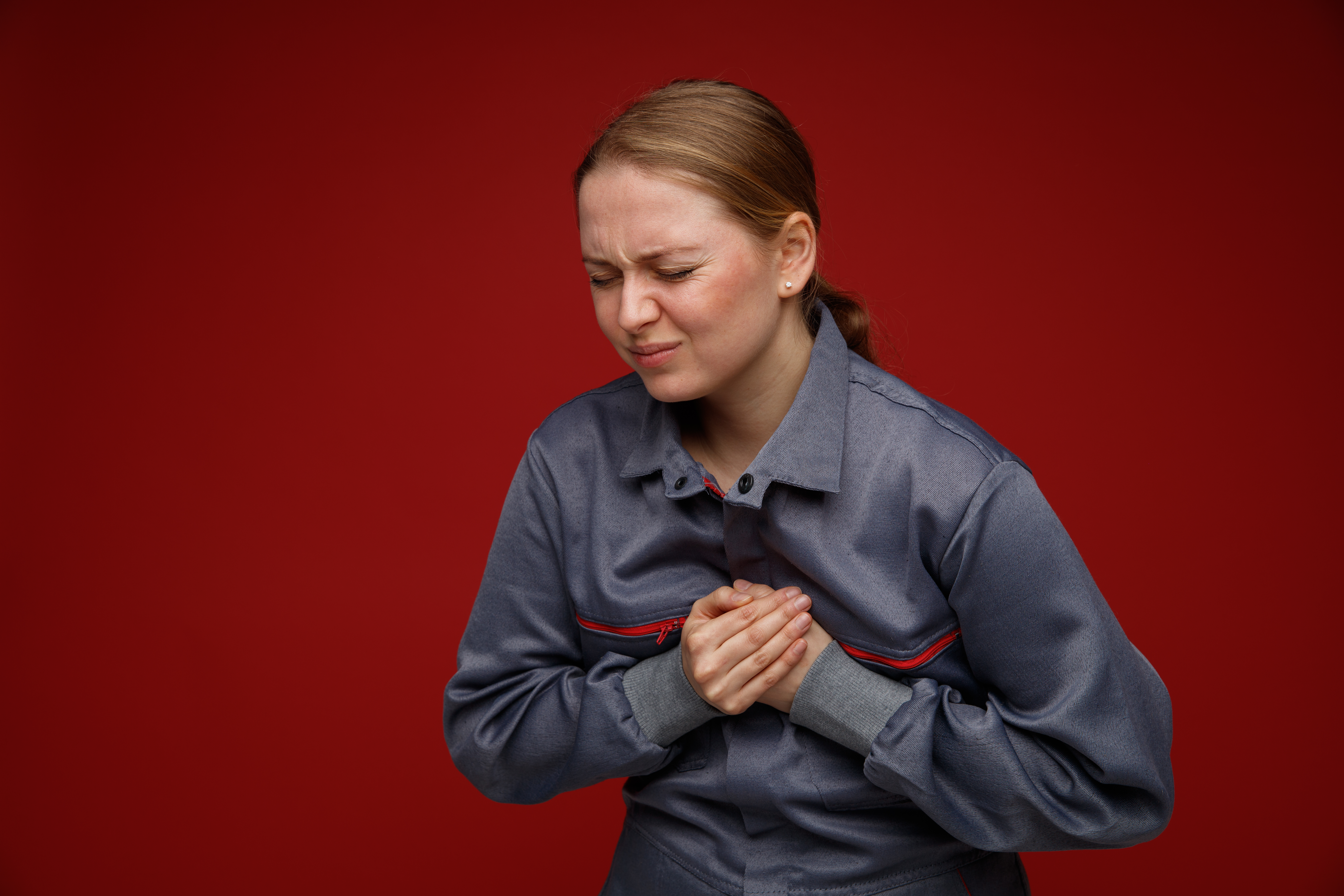 aching young blonde female engineer wearing uniform keeping hands on chest with closed eyes isolated on bordo background with copy space aching young blonde female engineer wearing uniform keeping hands on chest with closed eyes isolated on bordo background with copy space