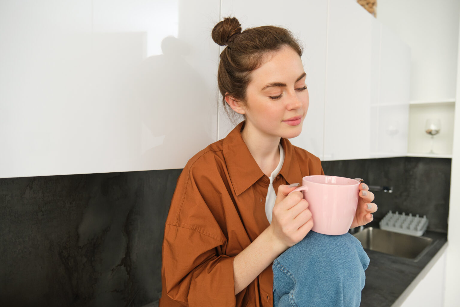 Portrait of beautiful young woman enjoying her morning cup of aromatic coffee, drinking tea while sitting in kitchen and contemplating sunny day Portrait of beautiful young woman enjoying her morning cup of aromatic coffee, drinking tea while sitting in kitchen and contemplating sunny day