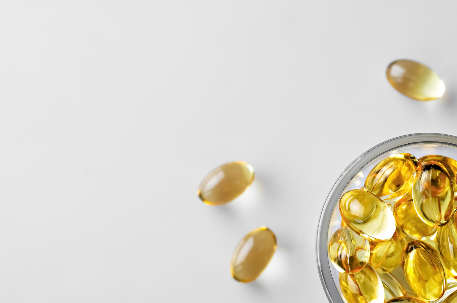 Capsules of fish oil (omega-3) in a glass bowl and on a white stschl nearby. Flat lay with copy space, white background. Capsules of fish oil (omega-3) in a glass bowl and on a white stschl nearby. Flat lay with copy space, white background.